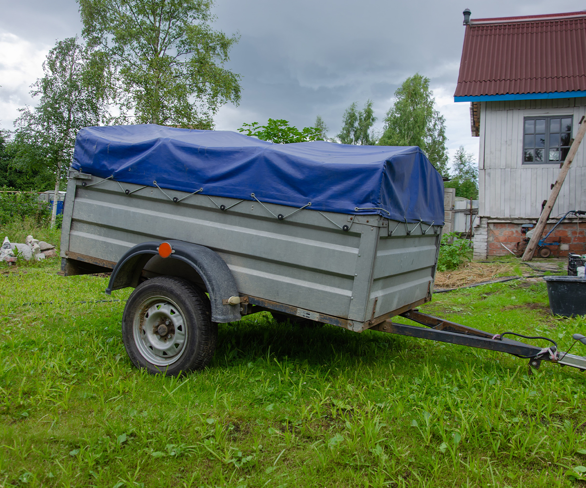 Farm utility trailer with tarp cover parked beside a barn